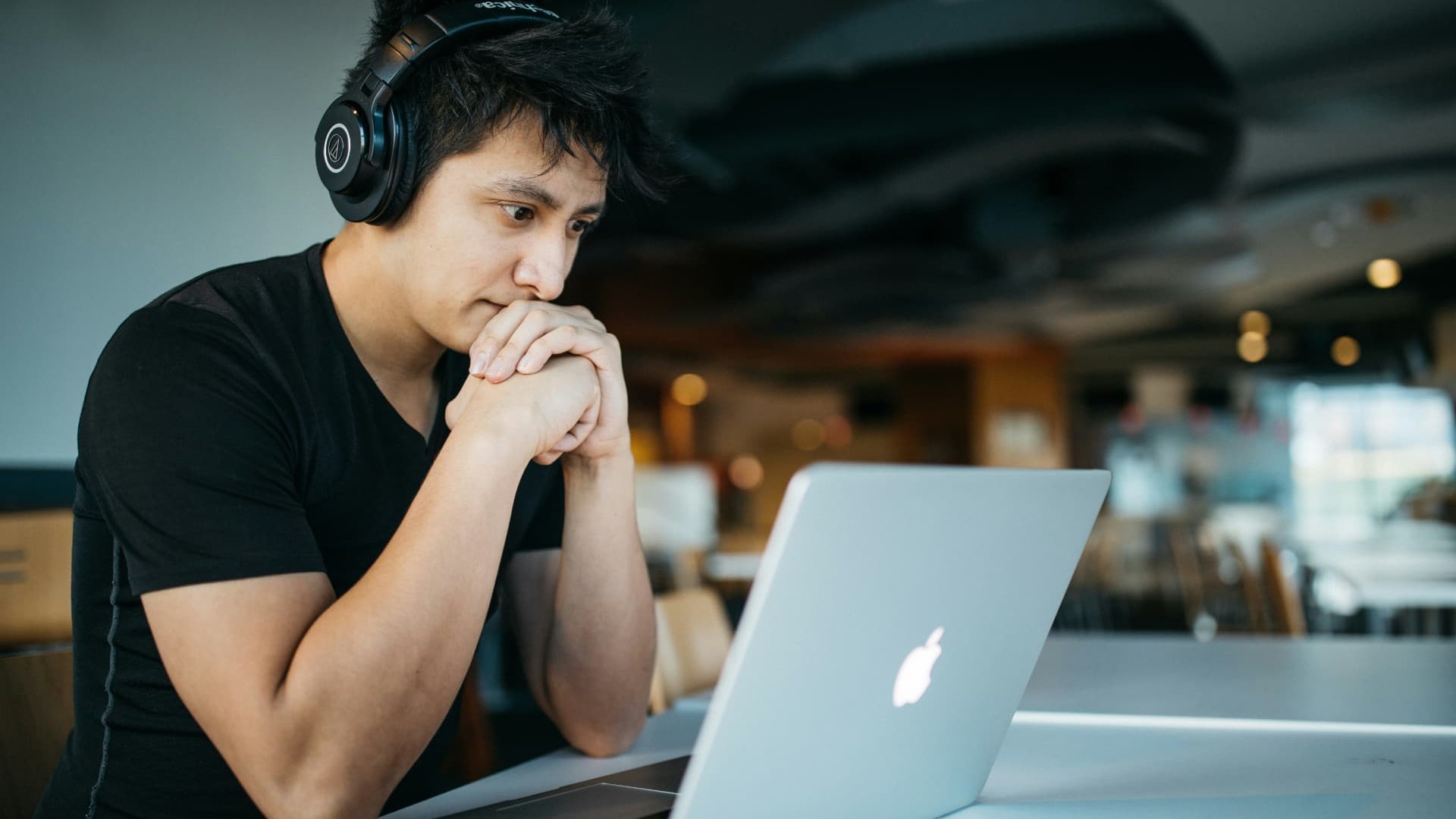 A student wearing headphones, leaning over a laptop during a live online class